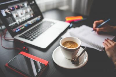 Desk with computer, coffee, and someone writing on a notepad