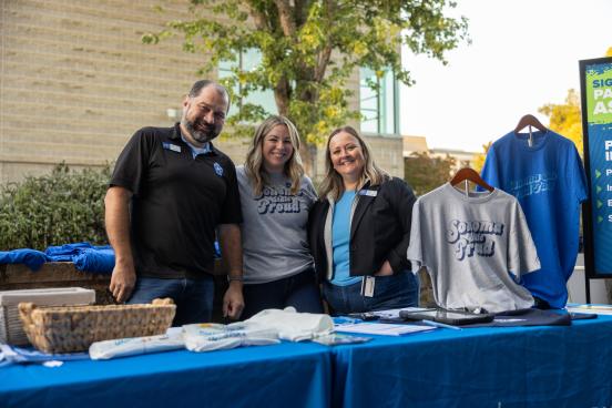 Three staff members standing outdoors, smiling at the camera, wearing Sonoma State University Mechandise
