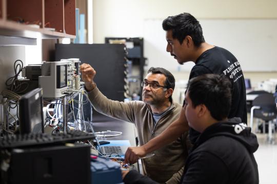 Three people staring at a device adjusting knobs in a computer lab