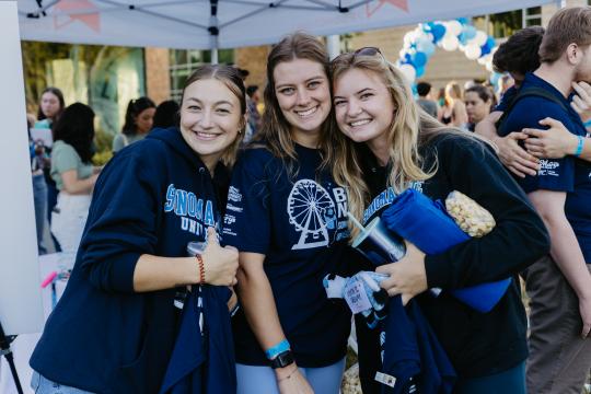 Three girls holding assorted Sonoma State University items smiling 
